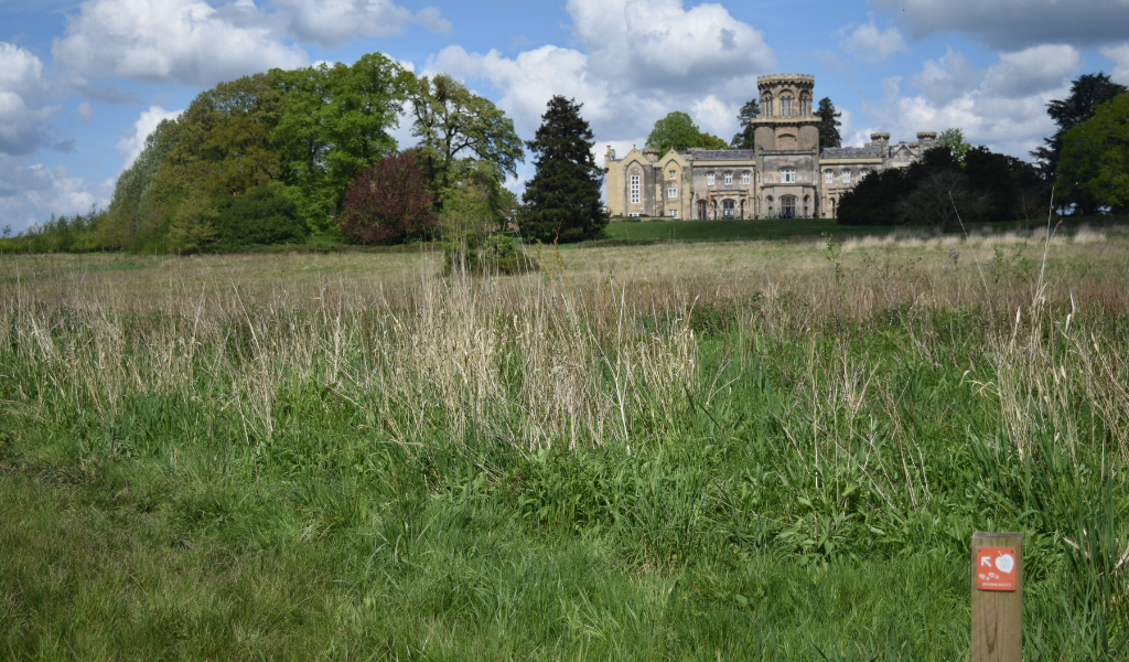 Studley Castle in the distance with an open field in front of it, and a waymarker post the bottom left.