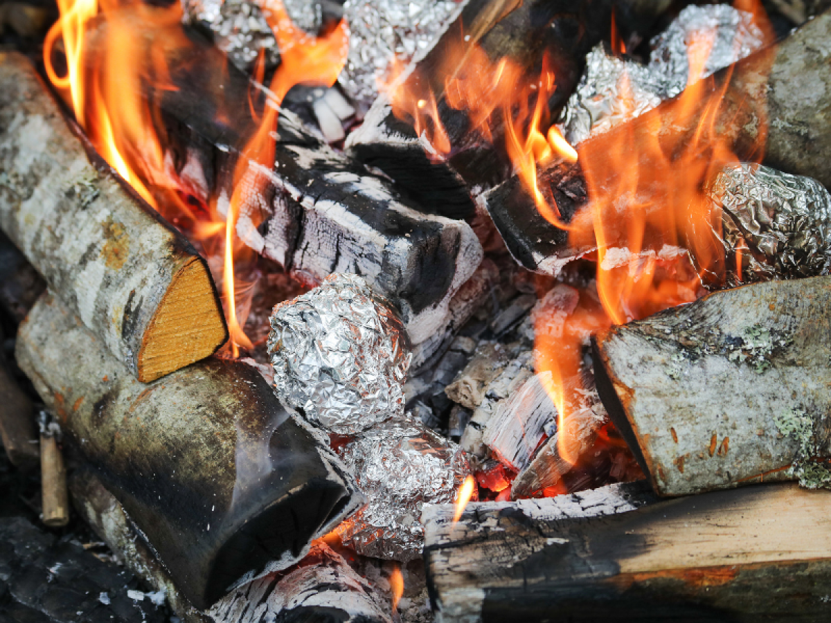 A close-up of a fire cooking potatoes wrapped in tinfoil