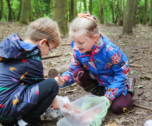 A couple of children knelt down looking at crafting supplies in the woods